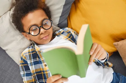 a boy with glasses reads a banned book on a pile of pillows