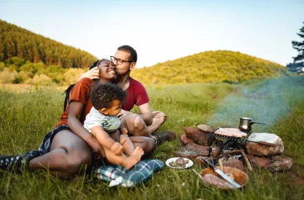 family cooks a meal over a fire while having fun camping