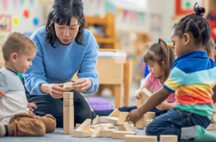 A teacher with kids in a day care playing with blocks 
