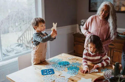 A family crafts snowflakes together in front of a window as a winter activity