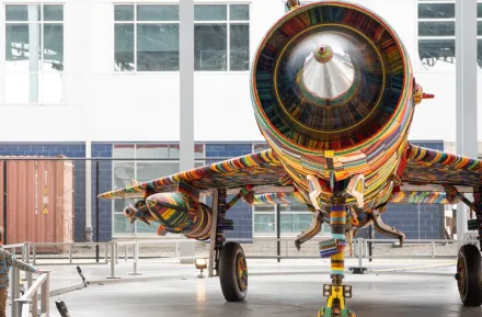 young boy walking underneath the wing of a fighter jet decorated with glass beads, part of “The MiG-21 Project” exhibit this weekend at The Museum of Flight