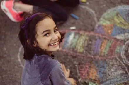 A young girl creates chalk art on the sidewalk.