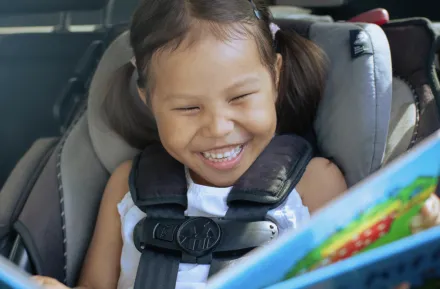 girl in a car seat with a fun car toy happy on a road trip