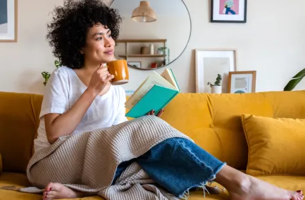 woman sitting on a couch with a cup of coffee and a book