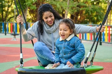 mom playing with child on swing at playground