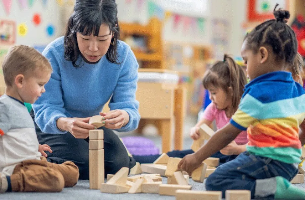 A teacher with kids in a day care playing with blocks 