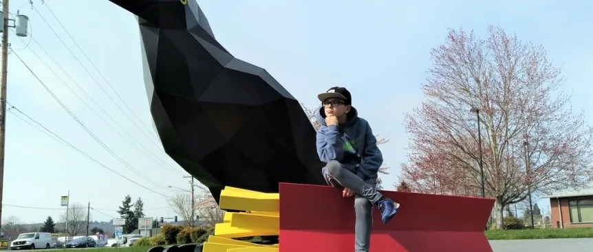 Young teenage boy in hat glasses sweatshirt seated on french fries of Auburn's Crow With Fries sculpture at Les Gove Park best instagram worth sites around Seattle