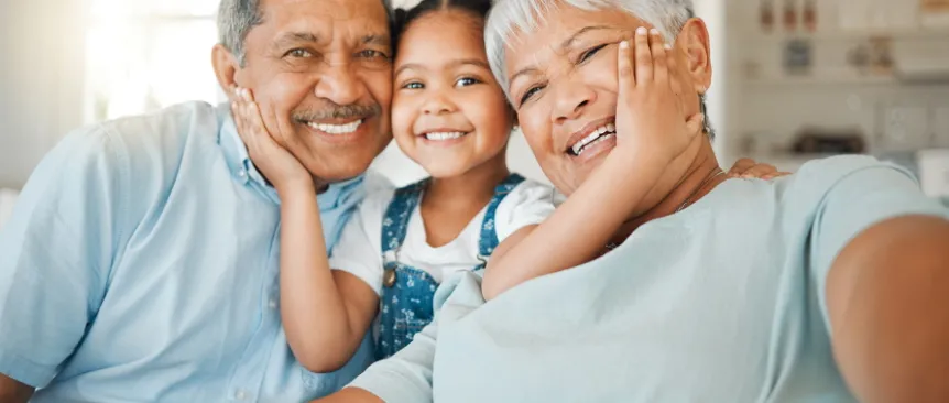 Child sitting between grandparents with her hands on their faces, all smiling