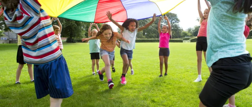 Kids holding up a parachute while two children run under it