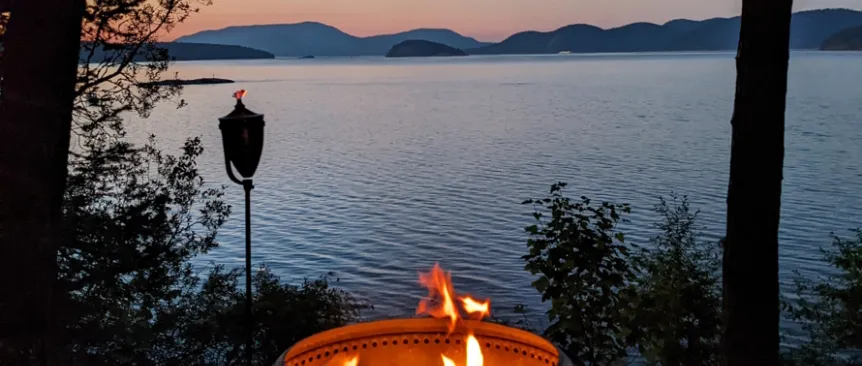 A fire in a fire pit near the water with mountains in the background
