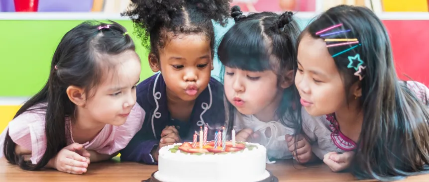 Little girls around a birthday cake blowing out the candles 