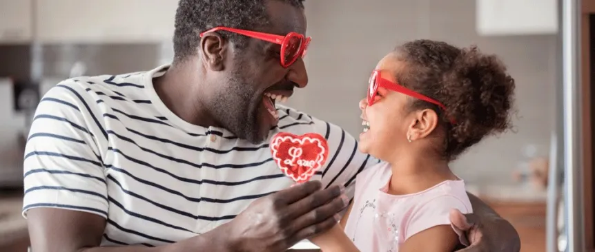 A dad and daughter wearing heart sunglasses, a useful valentine gift for kids while exchanging a red heart