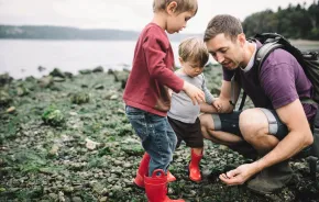 Dad and two little kids looking at rocky beach and tide pool finds at a Seattle beach