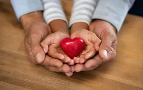 Adult and child hands holding a red heart