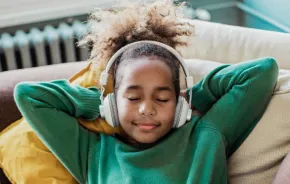 Young girl lying on a couch with eyes closed wearing headphones listening to a best podcasts for kids