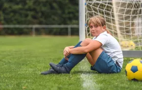 Girl sitting on the grass next to a soccer ball