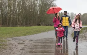 Family outside in the rain with two young girls riding scooters