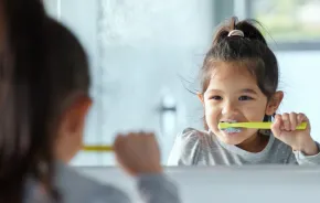 a little girl brushes her teeth in the mirror using tricks that helped her build a new habit