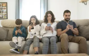 family sitting on a couch looking at their cell phones