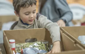 young boy putting food in a box at a food bank