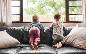 two kids sitting on a couch looking outside