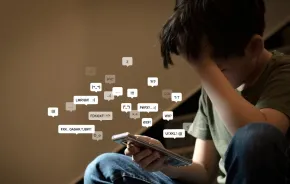 preteen boy covering his face with hands holding smartphone in low light