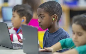 boy using a computer and ear buds in a classroom