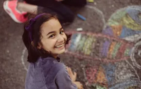 A young girl creates chalk art on the sidewalk.