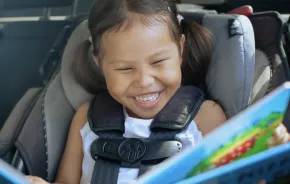 girl in a car seat with a fun car toy happy on a road trip