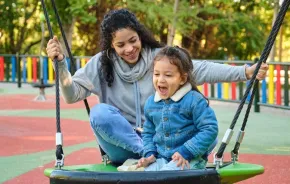 mom playing with child on swing at playground