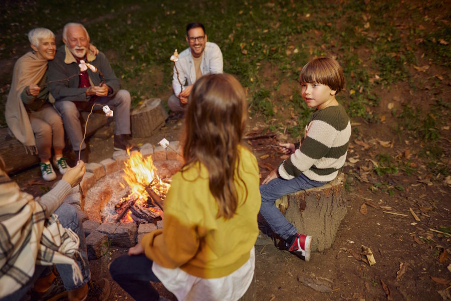 Happy multi-generation family enjoying roasting marshmallows around a campfire ready for campfire games.