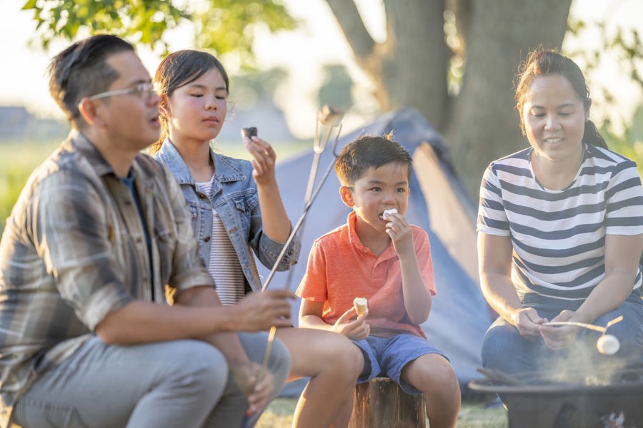 Family roasting marshmallows around campfire at a camp site ready to play campfire games