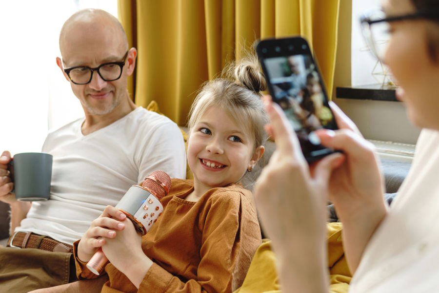daughter holding a microphone sitting next to dad on couch mom recording