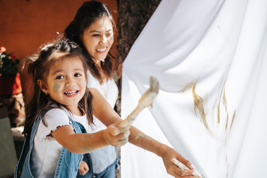 Girl and mom painting on a shower curtain outside 