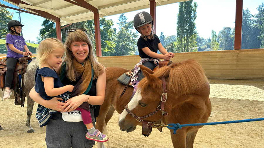 Smiling mom with kids on ponies during the fall festival Pumpkins and Ponies at Seattle Farm
