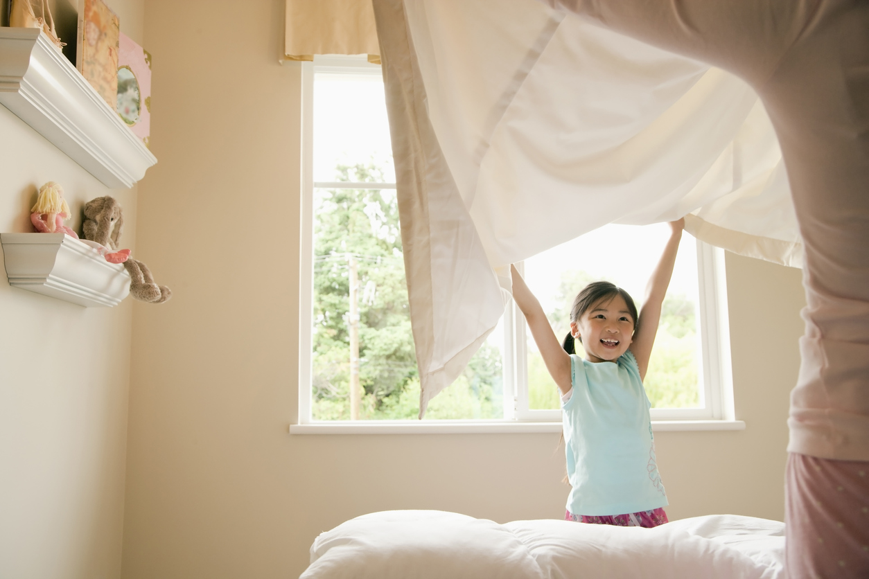 mother and daughter lifting a new bedding sheet onto a bed