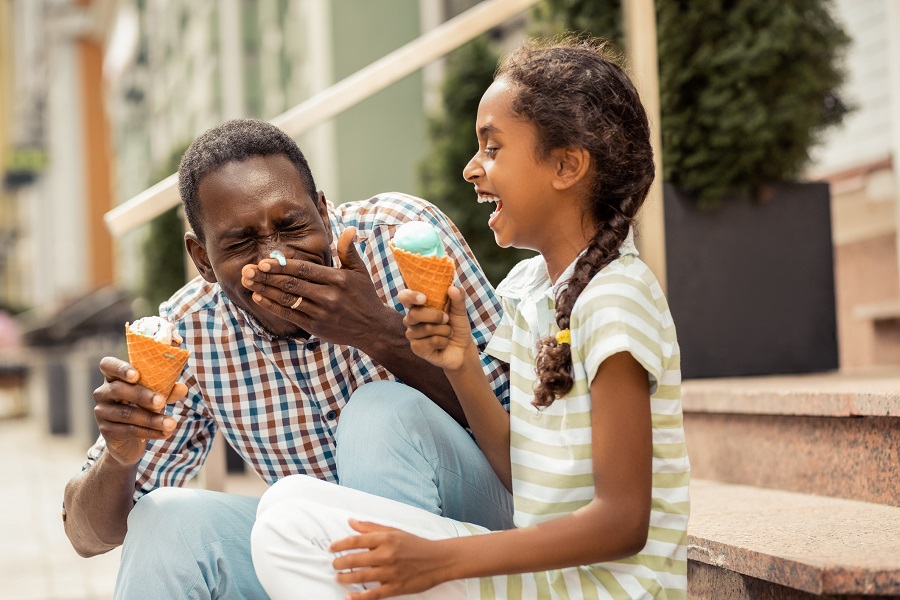 A dad and his young daughter laugh together while enjoying an ice cream cone