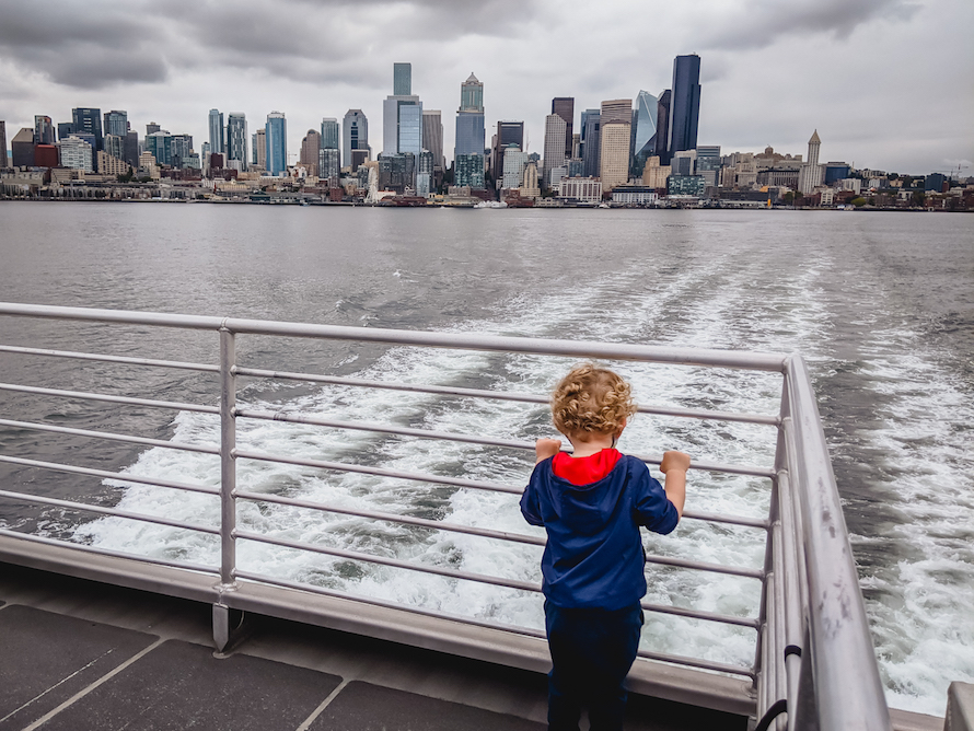 curly-haired blond boy looking at the Seattle skyline from the deck of the west seattle water taxi