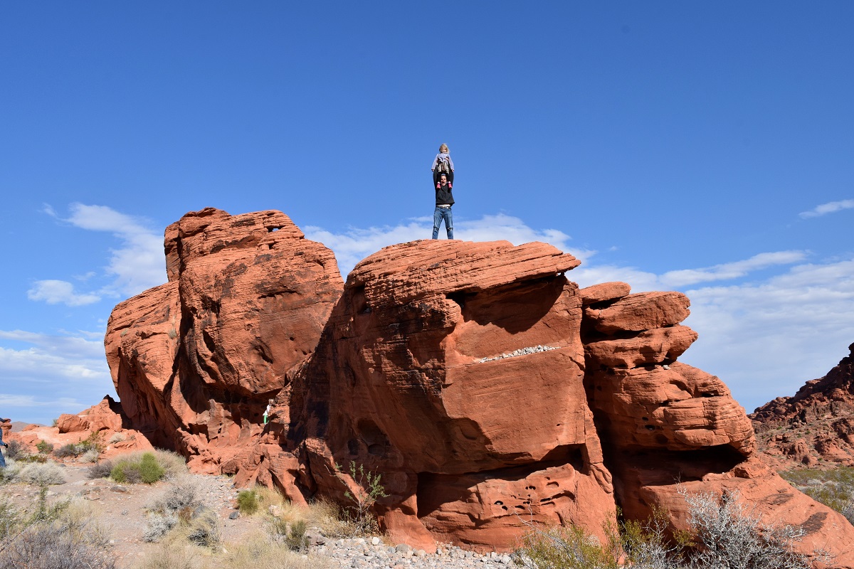 A dad with child on his shoulders poses on top of a rock formation at Valley of Fire near Las Vegas best sunny destinations one short flight from Seattle