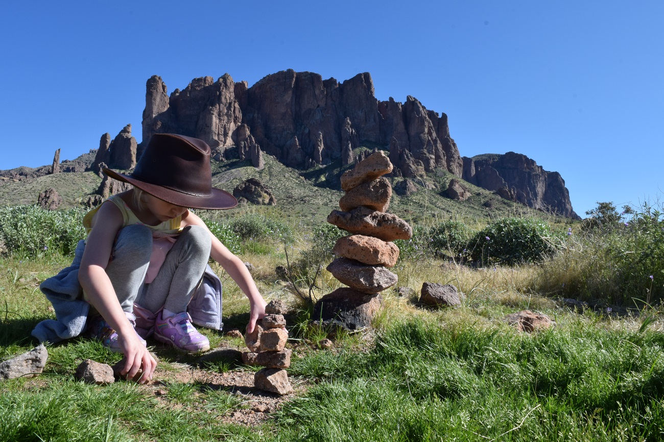 Young girl wearing hat is stacking rocks intently at Lost Dutchman State Park near Phoenix Arizona best sunny destinations one flight away from Seattle