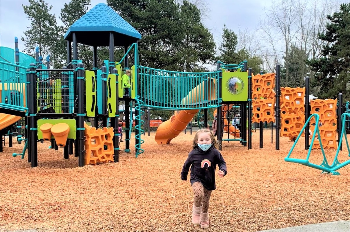 A young girl runs in front of a colorful new play structure at the new playground at Renton's Gene Coulon Memorial Beach Park near Seattle