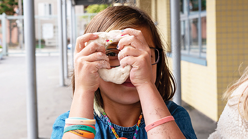Young girl at camp peeks through a hole in a dough circle