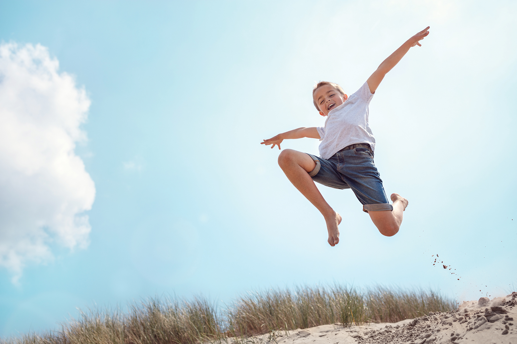 Adorable boy wearing shorts leaps into the air on a sunny day