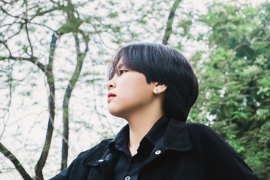 Asian American youth shown in profile in a park-like setting with trees in the background