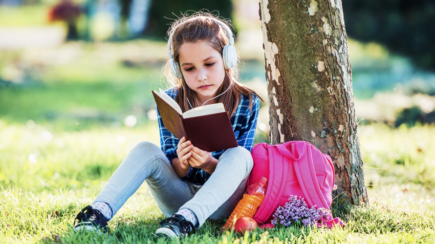 Girl sitting under a tree reading a middle grade book about women's history