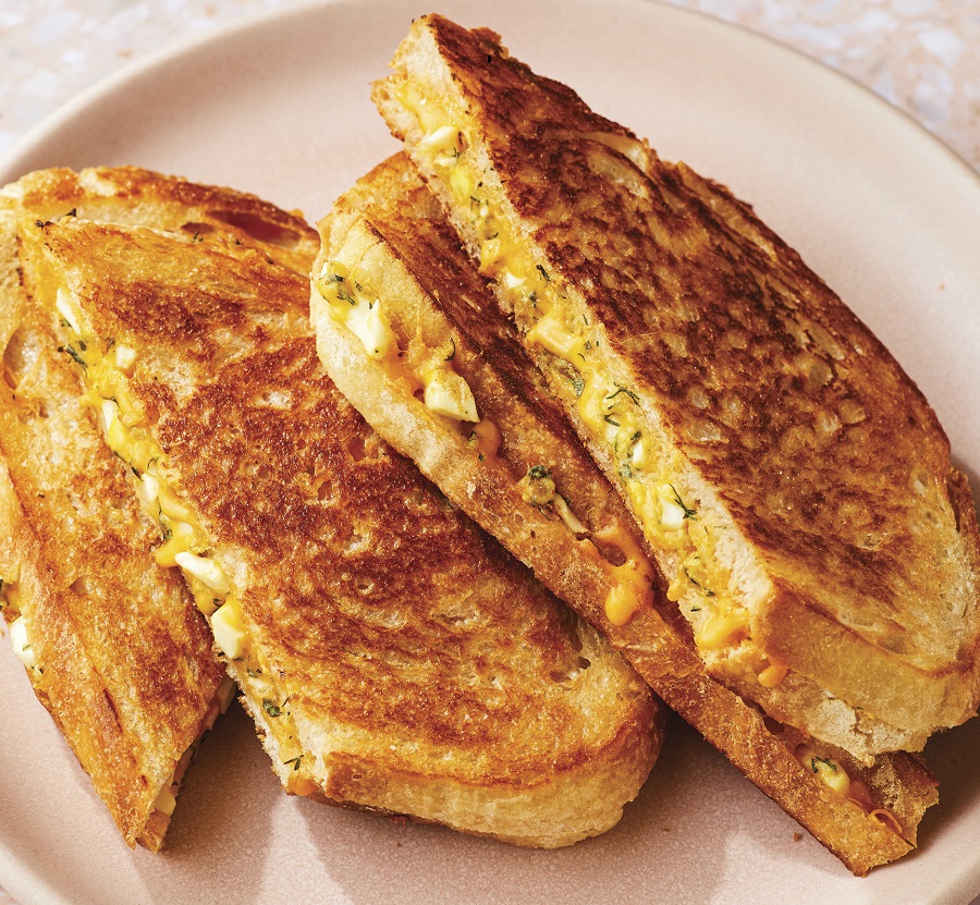A plate with a toasty, cheesy egg salad sandwich on it