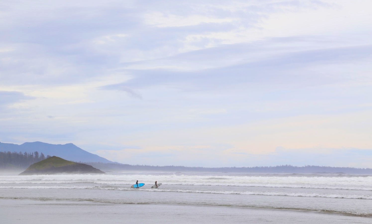 Two surfers walking on the beach in Tofino, B.C., a nearby pacific northwest road trip destination for seattle families