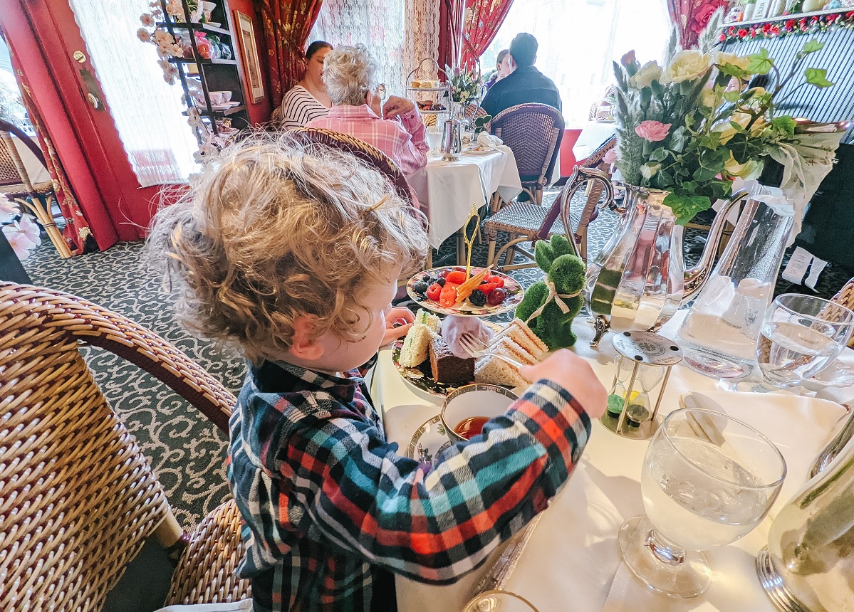 A young boy in a plaid shirt sits at a table and enjoys afternoon tea in Seattle with purple cotton candy, among many treats served to kids at the Queen Mary Tea Room in Seattle