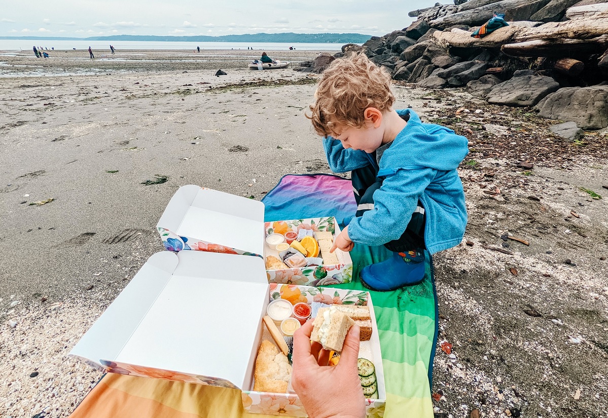 Boy standing on the beach with a box of treats from the Secret Garden Tea Room