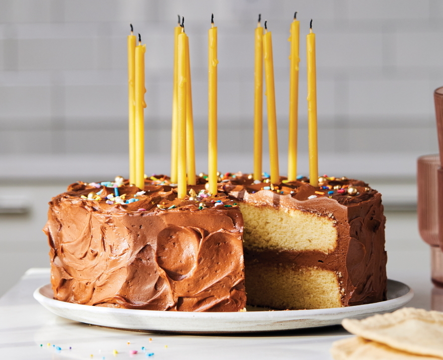Yellow birthday cake with tall yellow candles and chocolate frosting